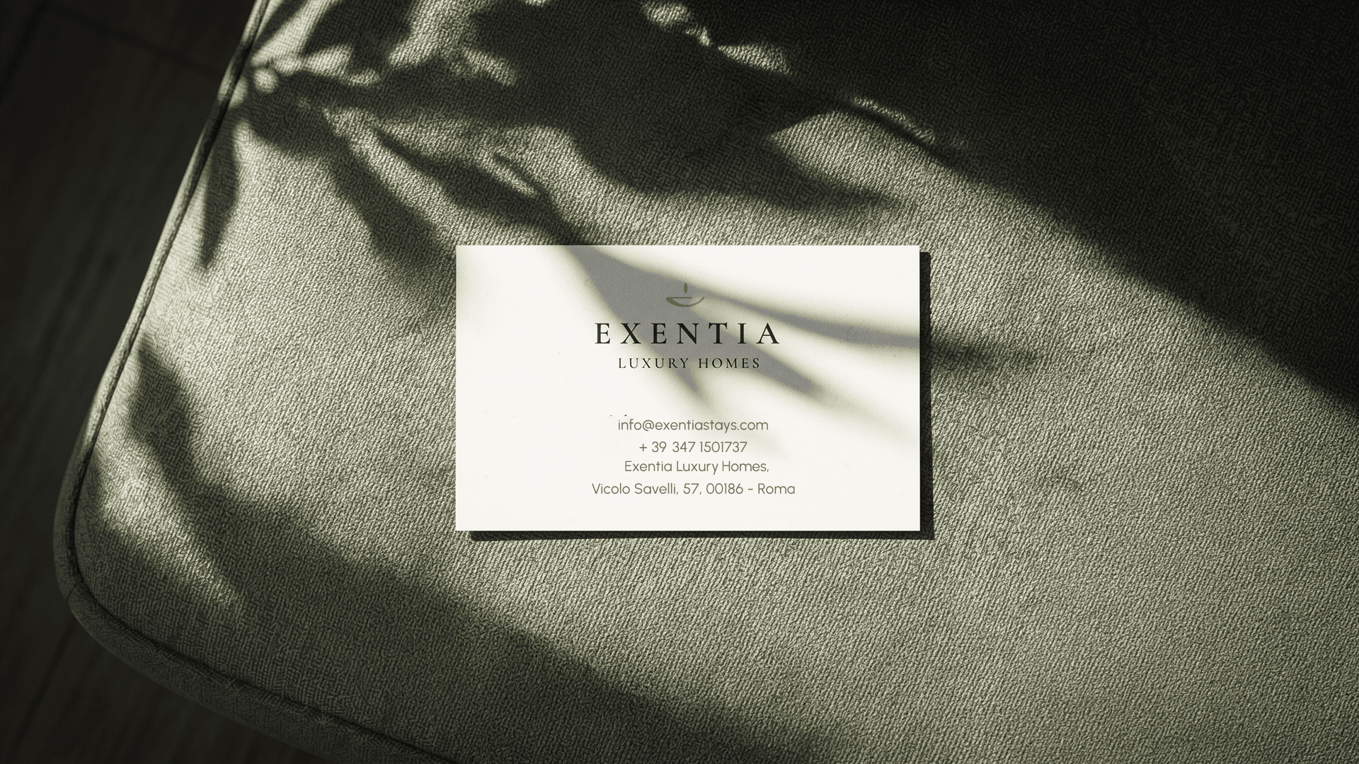 Exentia Luxury Stays business card on a green sofa in soft shadows