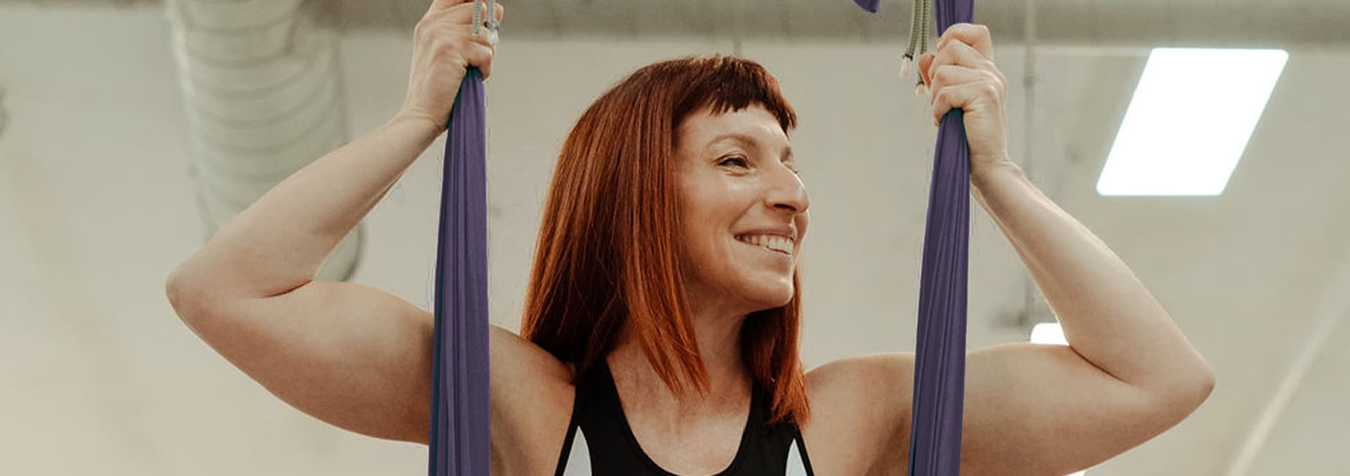 Smiling woman holding purple aerial yoga silks